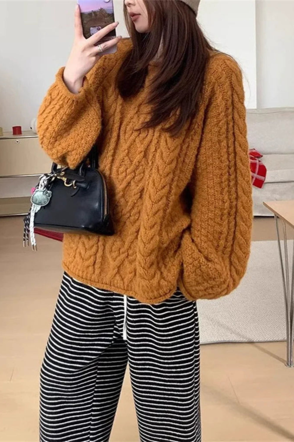 Person wearing a mustard yellow cable knit sweater and black and white striped pants, holding a black handbag.