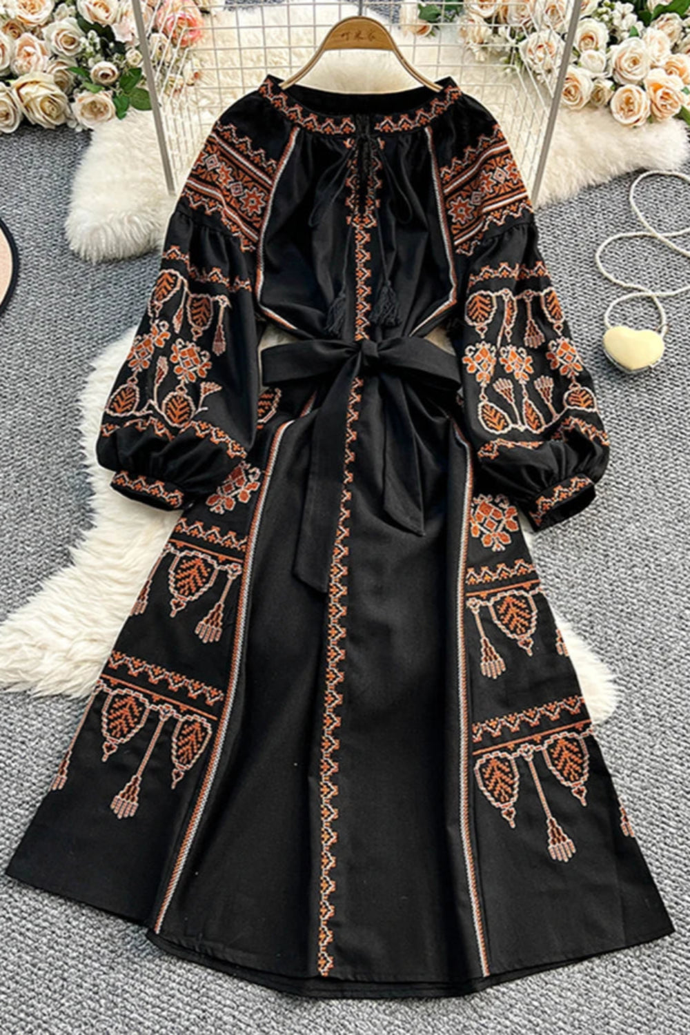 Black embroidered dress on a hanger with floral decorations in the background