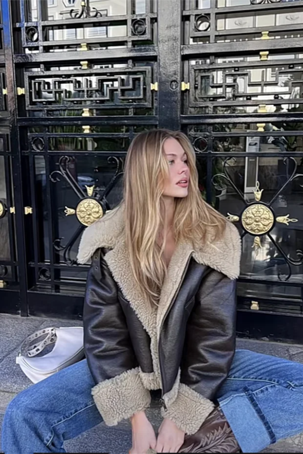 Person wearing a shearling jacket sitting in front of a decorative metal gate.