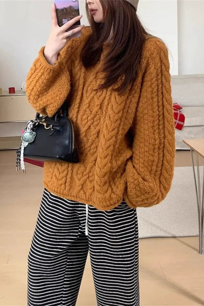Person wearing a mustard yellow cable knit sweater and black and white striped pants, holding a black handbag.