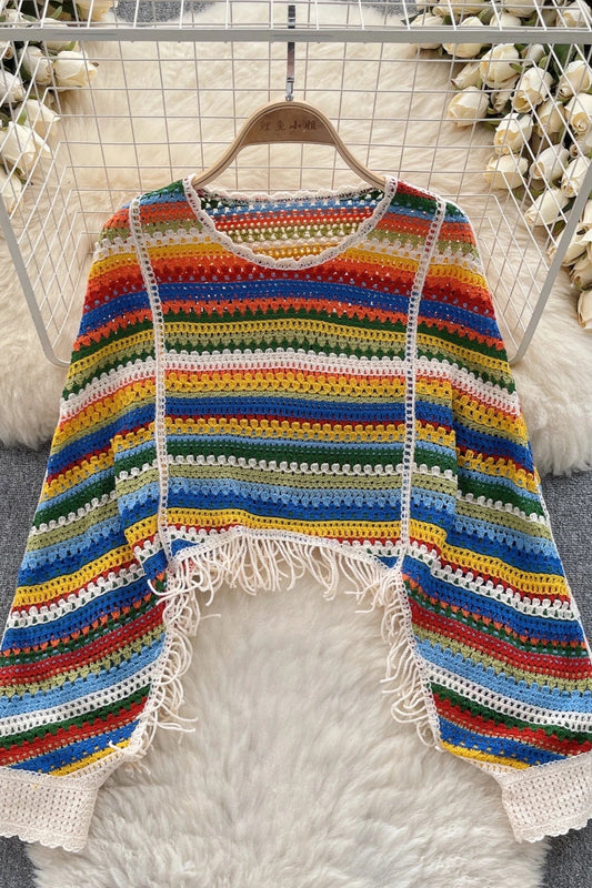 Colorful striped crochet sweater with tassels on a hanger against a floral and fur background.